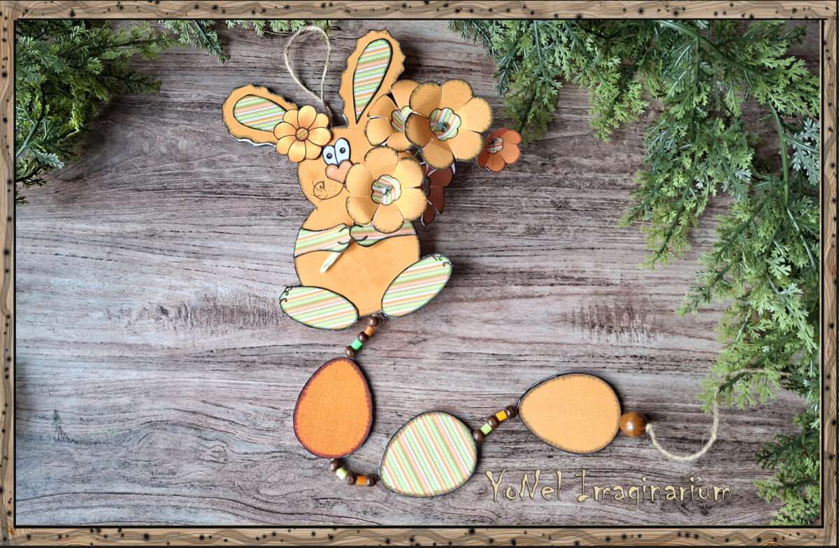 Handmade 3D printable Easter bunny wall hanging with layered paper flowers and decorative Easter eggs on a rustic wooden background.